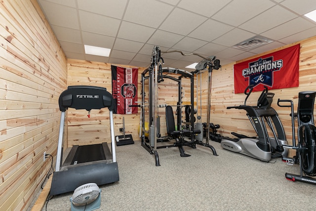 exercise room featuring a paneled ceiling, wooden walls, and carpet