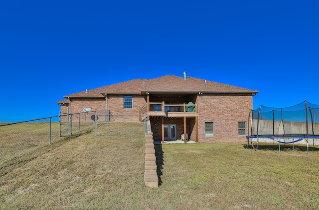 back of property with a balcony, a lawn, and a trampoline