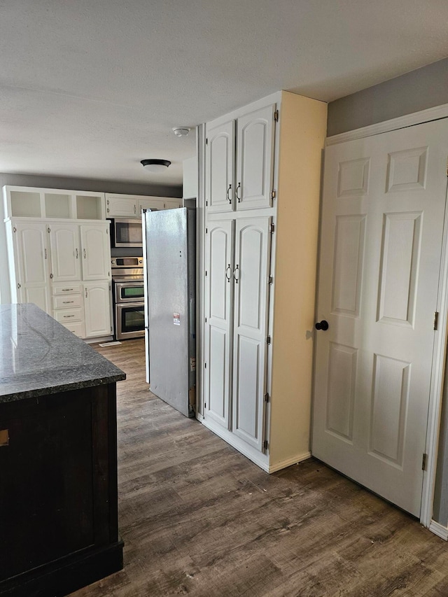 kitchen featuring stainless steel appliances, dark stone countertops, white cabinetry, and dark hardwood / wood-style floors