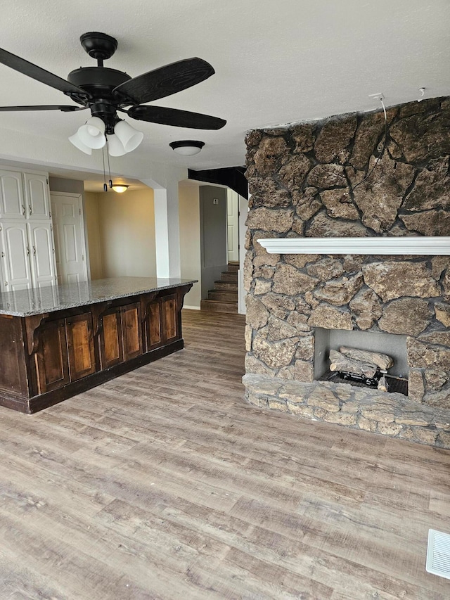 living room featuring ceiling fan, a stone fireplace, and light wood-type flooring