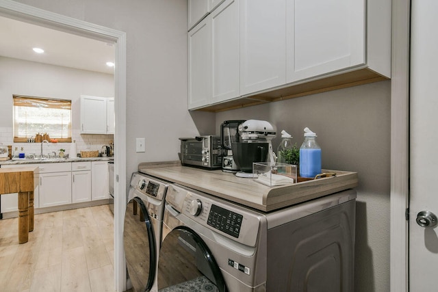 washroom with washing machine and dryer, cabinets, sink, and light hardwood / wood-style floors