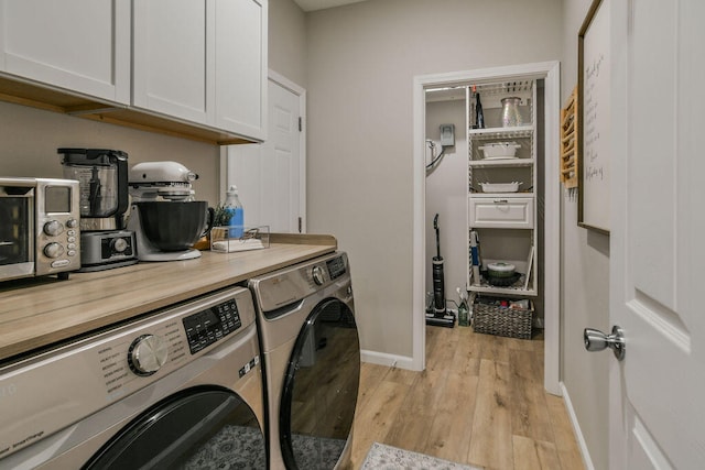 clothes washing area with washing machine and dryer, cabinets, and light hardwood / wood-style floors