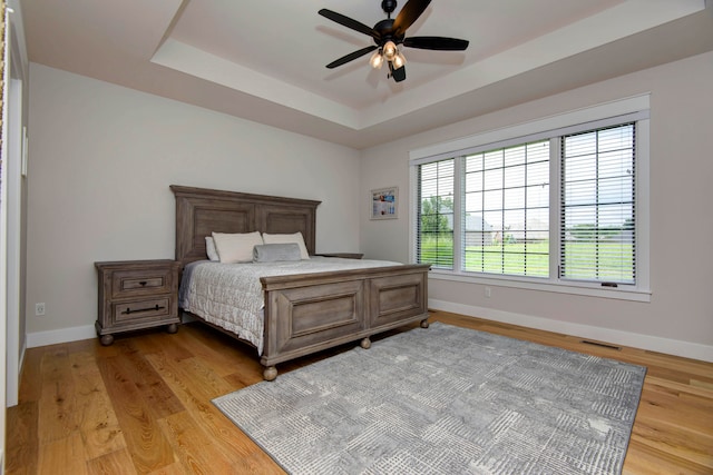 bedroom featuring ceiling fan, light wood-type flooring, and a tray ceiling