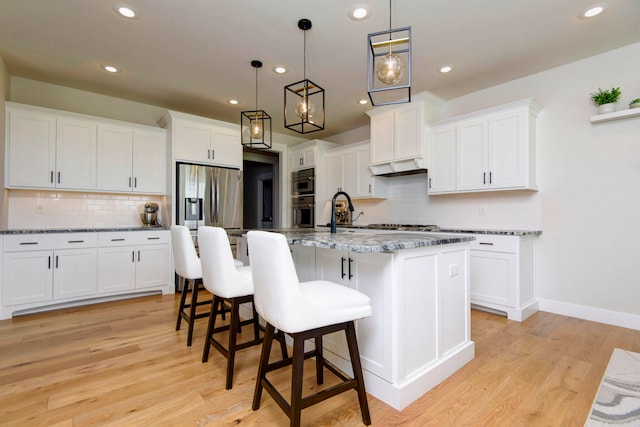 kitchen featuring light hardwood / wood-style floors, a center island with sink, custom exhaust hood, white cabinets, and pendant lighting