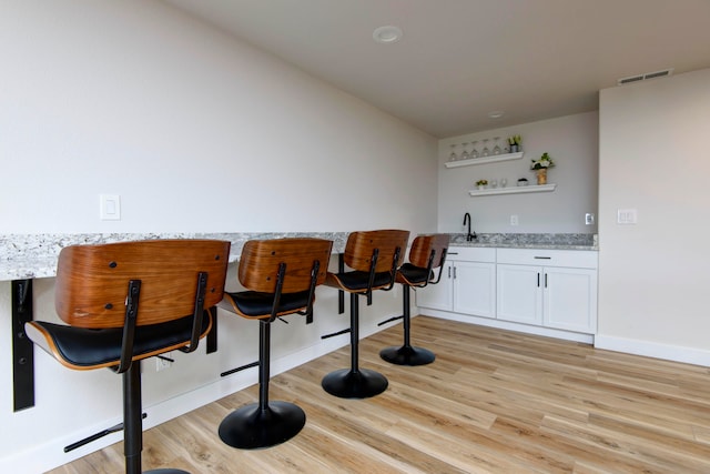 bar with light stone countertops, white cabinetry, sink, and light wood-type flooring