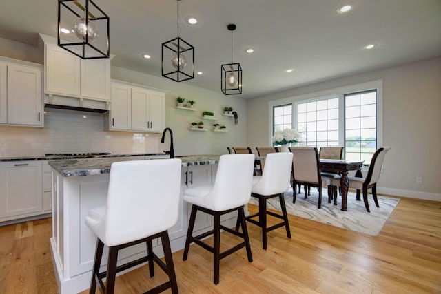 kitchen with a center island with sink, decorative light fixtures, white cabinetry, and light hardwood / wood-style flooring