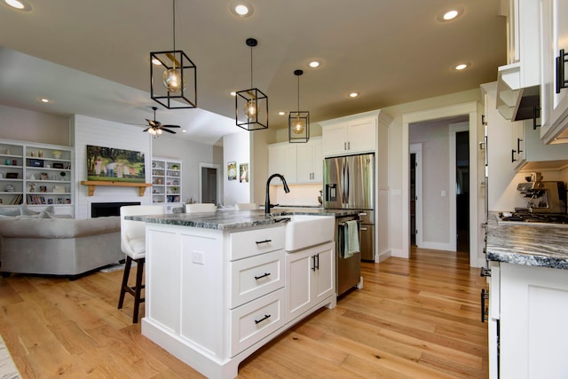 kitchen featuring dark stone counters, white cabinetry, pendant lighting, dishwasher, and a kitchen island with sink