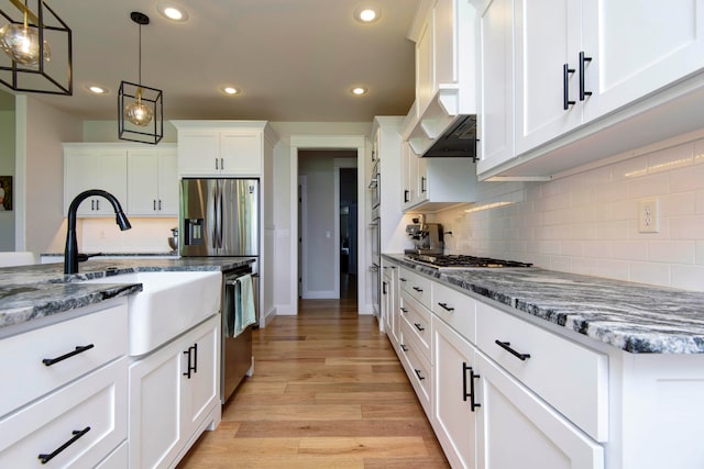 kitchen featuring appliances with stainless steel finishes, dark stone countertops, decorative light fixtures, white cabinets, and light wood-type flooring