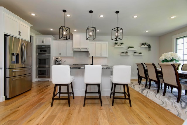 kitchen with stainless steel appliances, hanging light fixtures, white cabinetry, and a breakfast bar