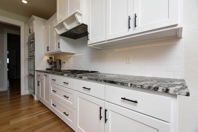 kitchen featuring white cabinetry, appliances with stainless steel finishes, tasteful backsplash, dark stone counters, and light wood-type flooring