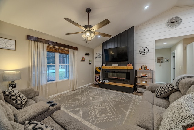 living room with wood walls, ceiling fan, lofted ceiling, and a large fireplace