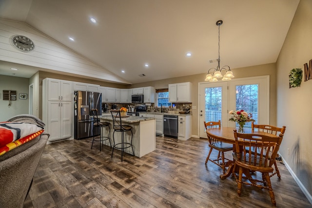 kitchen with appliances with stainless steel finishes, decorative light fixtures, dark hardwood / wood-style floors, light stone countertops, and a center island