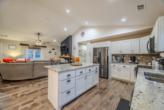 kitchen with stainless steel appliances, lofted ceiling, white cabinetry, and light stone counters