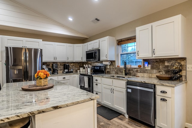 kitchen with appliances with stainless steel finishes, vaulted ceiling, and white cabinets