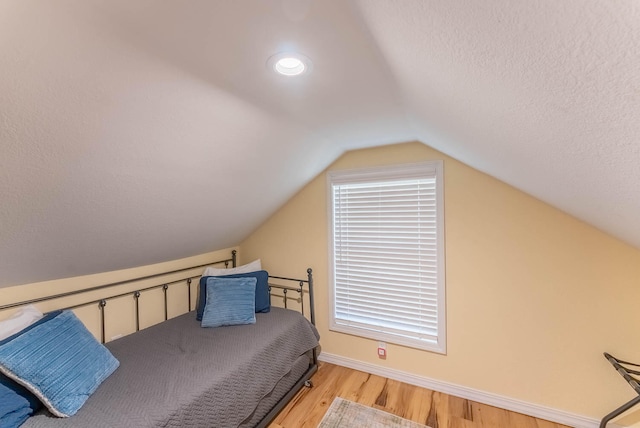 bedroom featuring a textured ceiling, light wood-type flooring, and vaulted ceiling