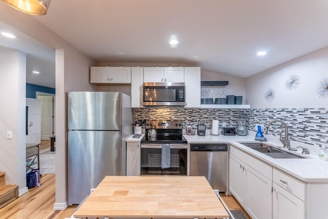 kitchen featuring stainless steel appliances, light wood-type flooring, decorative backsplash, white cabinets, and lofted ceiling