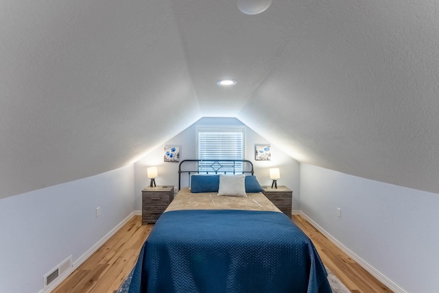 bedroom featuring wood-type flooring, a textured ceiling, and vaulted ceiling