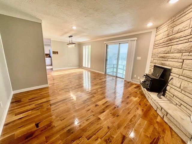 unfurnished living room with a textured ceiling, ornamental molding, hardwood / wood-style flooring, and a stone fireplace