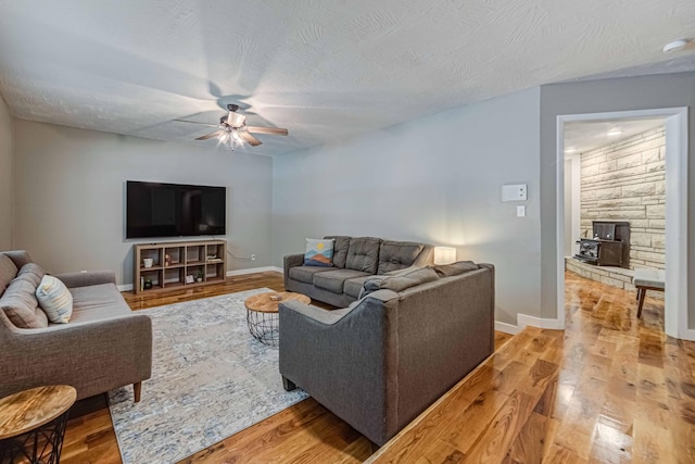 living room featuring a wood stove, hardwood / wood-style floors, ceiling fan, and a textured ceiling