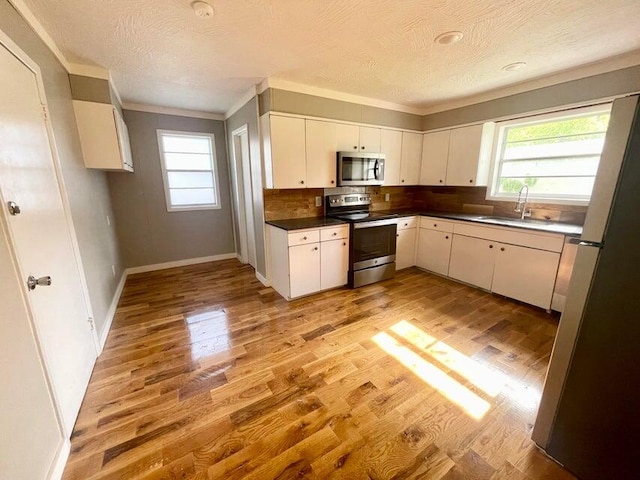 kitchen featuring white cabinets, sink, tasteful backsplash, light wood-type flooring, and appliances with stainless steel finishes