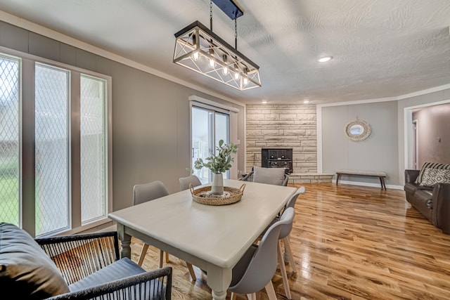 dining area featuring a fireplace, a textured ceiling, ornamental molding, and light hardwood / wood-style flooring