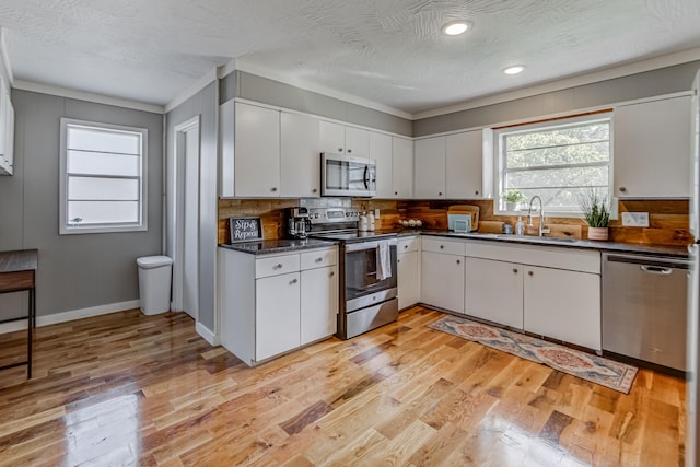 kitchen featuring stainless steel appliances, light hardwood / wood-style floors, white cabinetry, sink, and ornamental molding