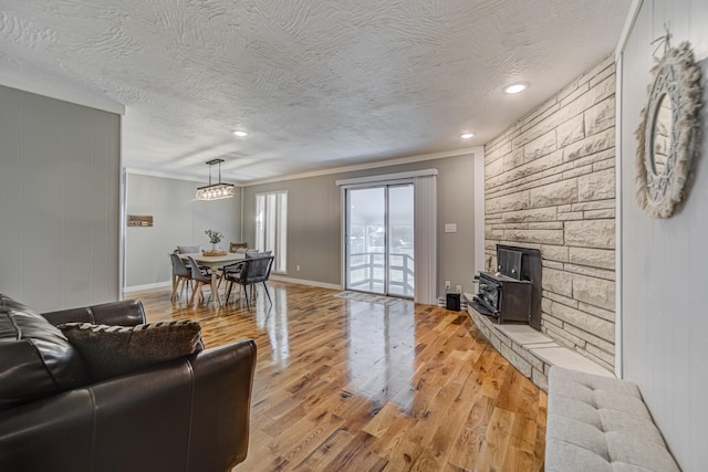 living room featuring a stone fireplace, light wood-type flooring, a textured ceiling, and ornamental molding