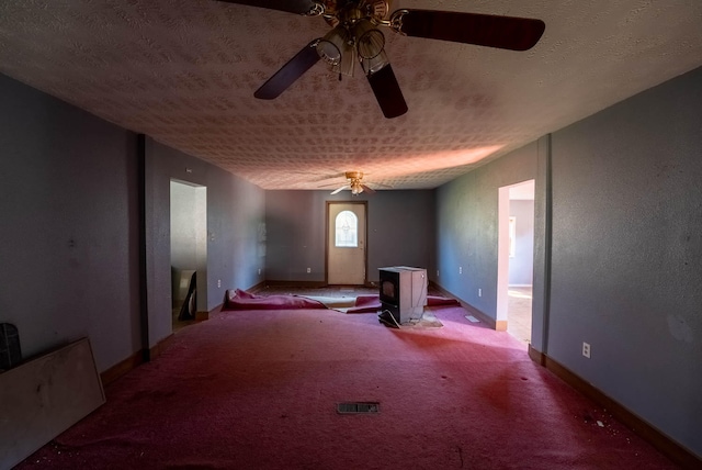 interior space with a wood stove, a textured ceiling, carpet floors, and ceiling fan