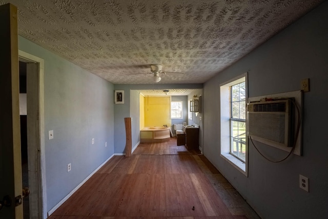 interior space featuring a textured ceiling, hardwood / wood-style flooring, ceiling fan, and a wall mounted air conditioner