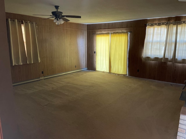 carpeted spare room with a baseboard radiator, wooden walls, and ceiling fan