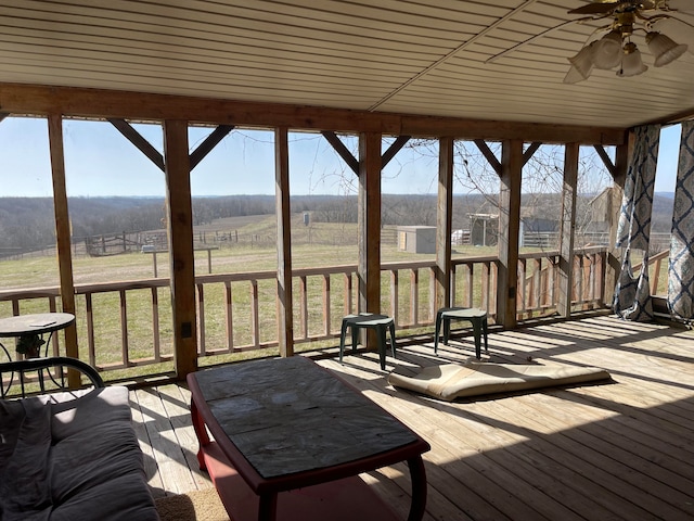 unfurnished sunroom with a wealth of natural light, ceiling fan, wood ceiling, and a rural view