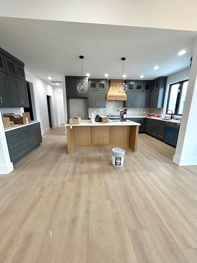 kitchen featuring hanging light fixtures, light hardwood / wood-style flooring, backsplash, an island with sink, and custom exhaust hood