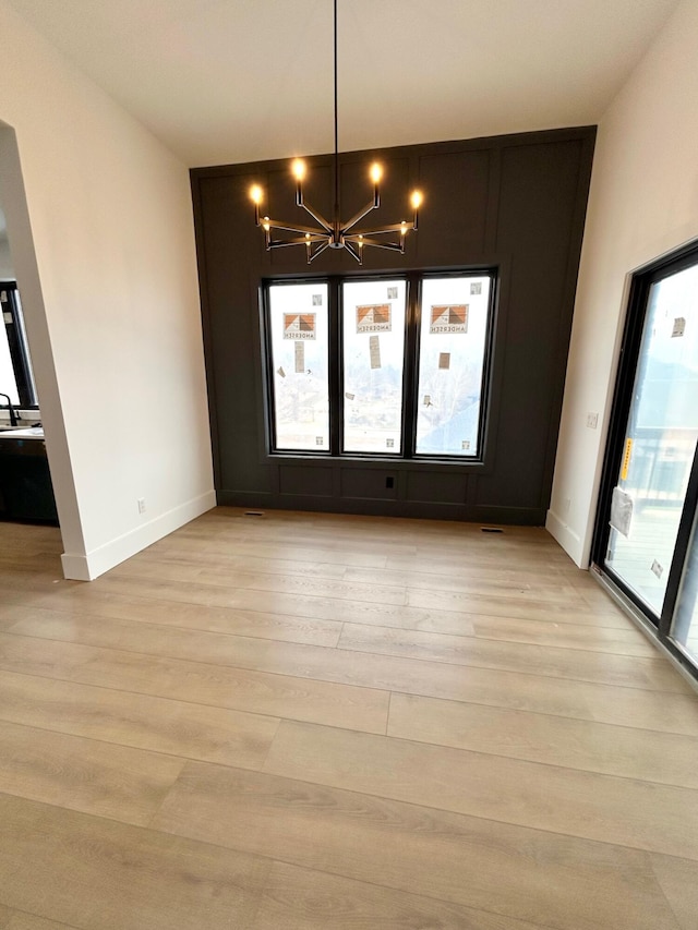 unfurnished dining area featuring a chandelier and light hardwood / wood-style flooring