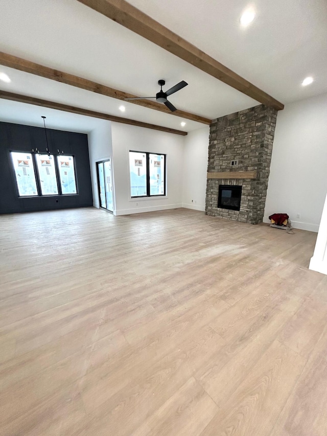 unfurnished living room with ceiling fan with notable chandelier, beam ceiling, a stone fireplace, and light wood-type flooring