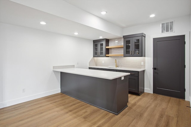 kitchen featuring decorative backsplash, kitchen peninsula, sink, and light hardwood / wood-style flooring