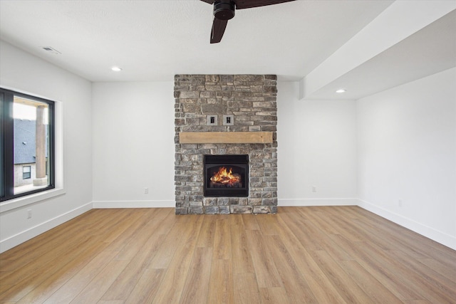 unfurnished living room with ceiling fan, a stone fireplace, and light hardwood / wood-style floors