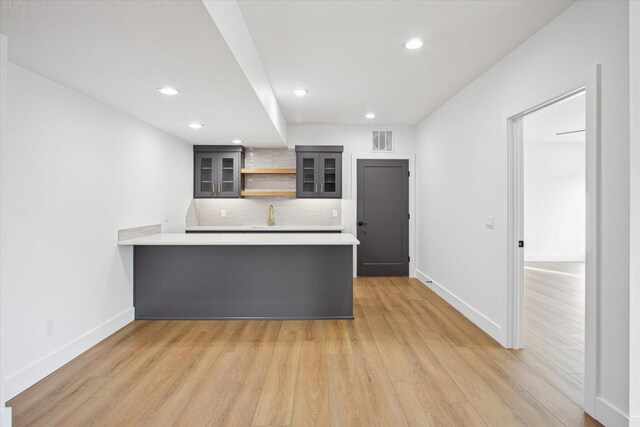 kitchen with sink, kitchen peninsula, light hardwood / wood-style floors, and backsplash