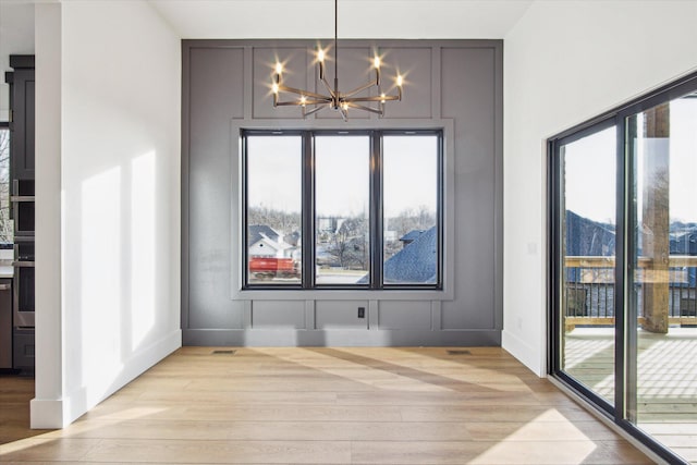 unfurnished dining area with a notable chandelier and light wood-type flooring