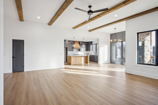 unfurnished living room with beamed ceiling, ceiling fan with notable chandelier, and light wood-type flooring