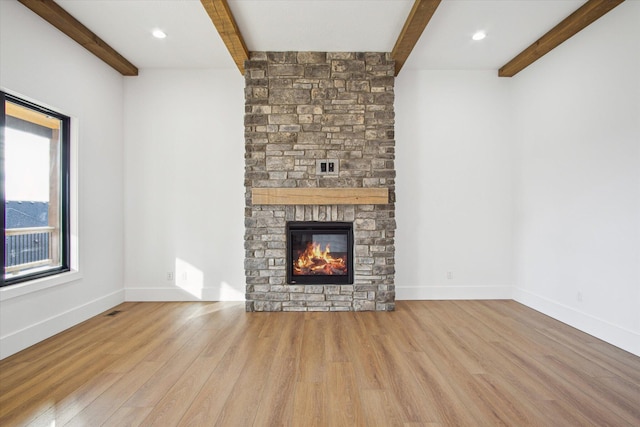 unfurnished living room featuring beam ceiling, a stone fireplace, and light hardwood / wood-style floors