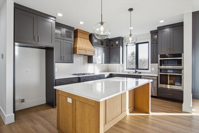 kitchen featuring sink, dishwasher, a center island, custom range hood, and decorative light fixtures