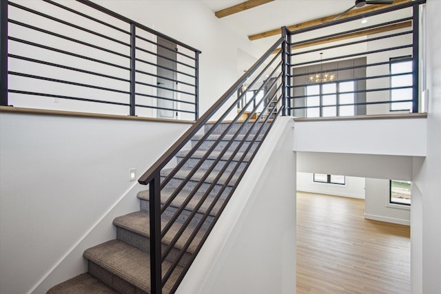 staircase featuring a towering ceiling, wood-type flooring, a chandelier, and beamed ceiling