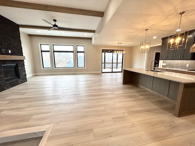 kitchen with a stone fireplace, sink, beamed ceiling, and pendant lighting