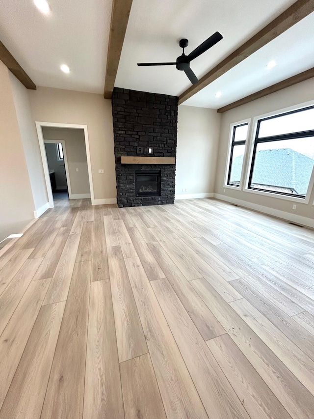 unfurnished living room with ceiling fan, beam ceiling, a fireplace, and light hardwood / wood-style flooring