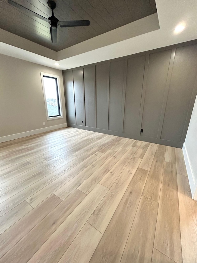 empty room featuring a raised ceiling, ceiling fan, wood ceiling, and light wood-type flooring