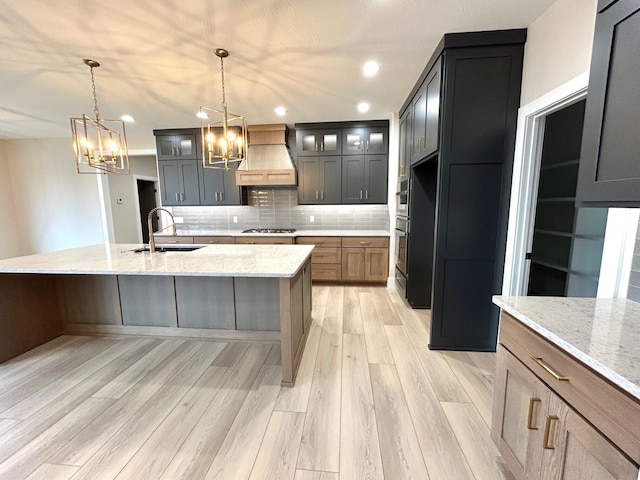 kitchen with custom exhaust hood, decorative backsplash, light stone countertops, and decorative light fixtures