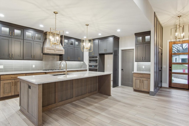 kitchen with a notable chandelier, light stone counters, a sink, light wood finished floors, and custom range hood