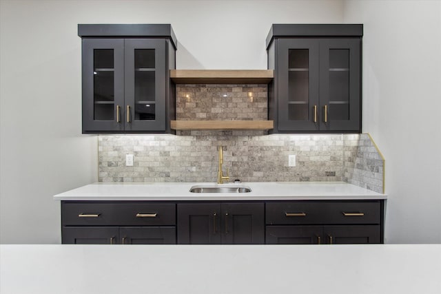 kitchen with glass insert cabinets, a sink, open shelves, and decorative backsplash