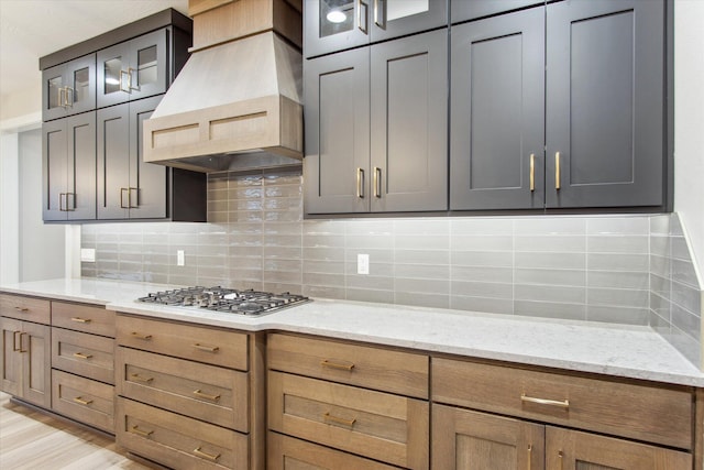 kitchen with decorative backsplash, glass insert cabinets, custom exhaust hood, and light stone counters