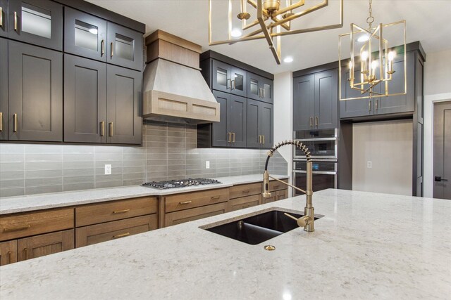 kitchen with stainless steel appliances, premium range hood, a sink, and a chandelier